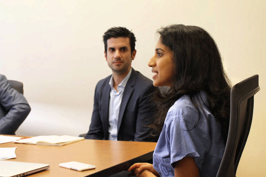 A small group in a business meeting setting, with individuals in formal attire seated at a conference table with papers and a laptop.