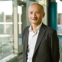 A person in a suit standing in a bright office environment with large windows.