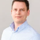 A person in a striped shirt is posing for a headshot against a plain background.