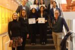 A group of people standing on stairs in a modern building. Three individuals hold certificates labeled "Y-Prize Winners." The setting appears formal.