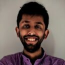 Headshot of person smiling, wearing a purple shirt against a neutral background.